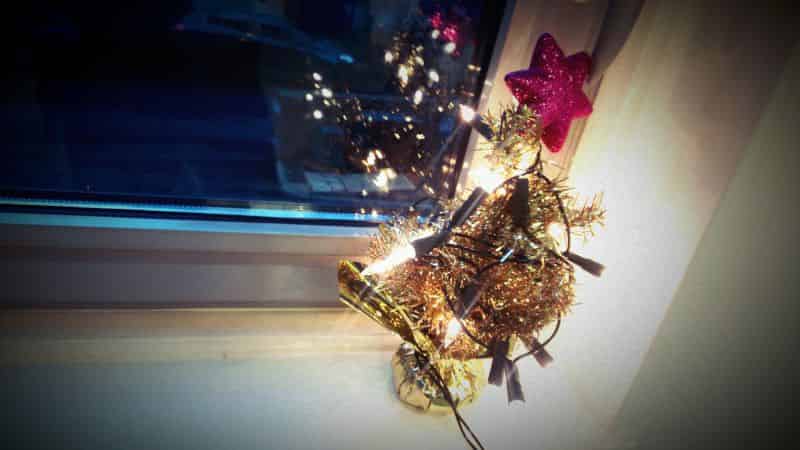 One-foot Christmas tree on a windowsil with oversized fairy lights and a topper. 