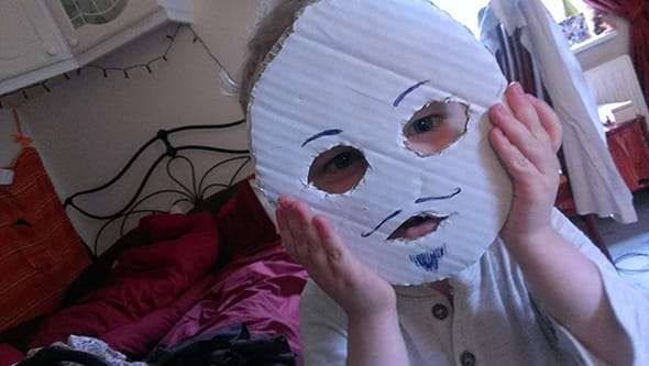Lucien holding a makeshift anonymous mask in front of his face.