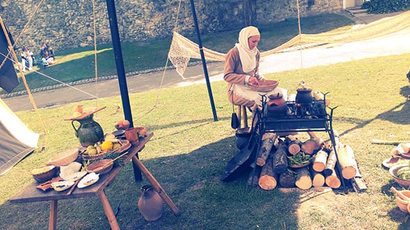 A woman dressed head to toe in medieval clothing making food at Rochester Castle.