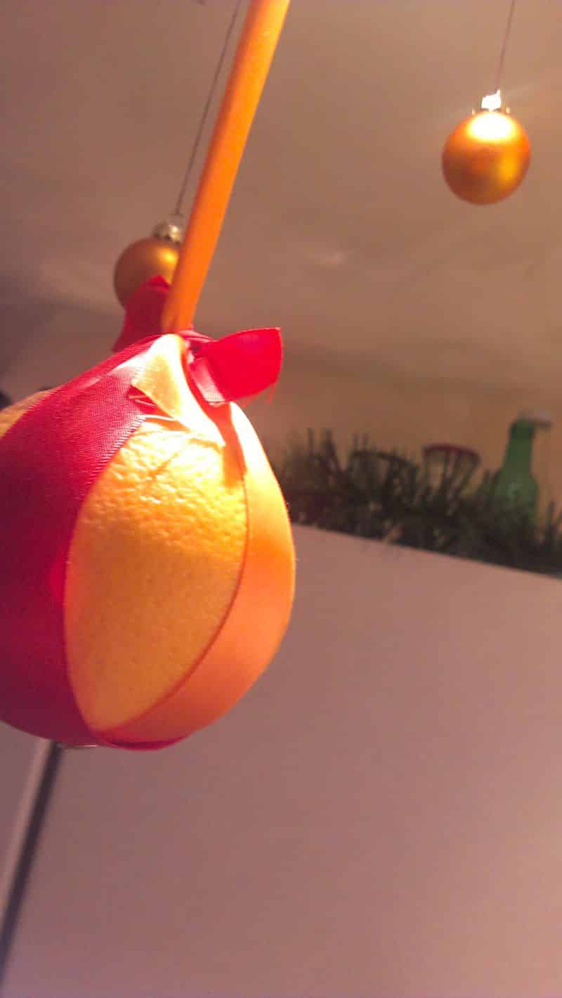 Orange, without cloves, hanging from the ceiling with red ribbon.