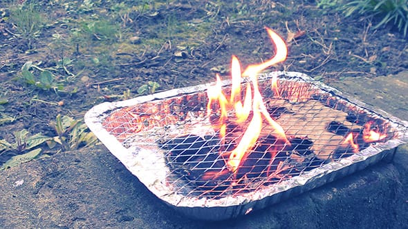 Fire spewing out from a tiny single-use barbecue, the kind you can buy at the gas station.