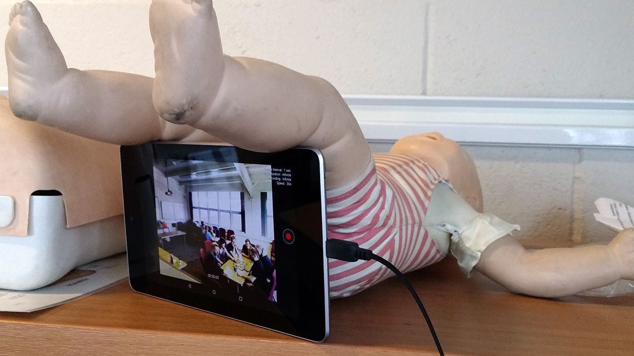 Resuscitation doll propped up to hold a tablet between its legs.