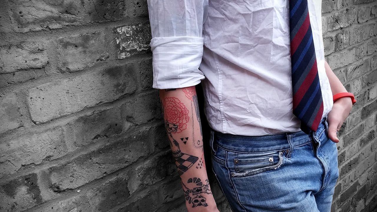 Carlos Eriksson standing against a brickwall showing his tattoed arm.