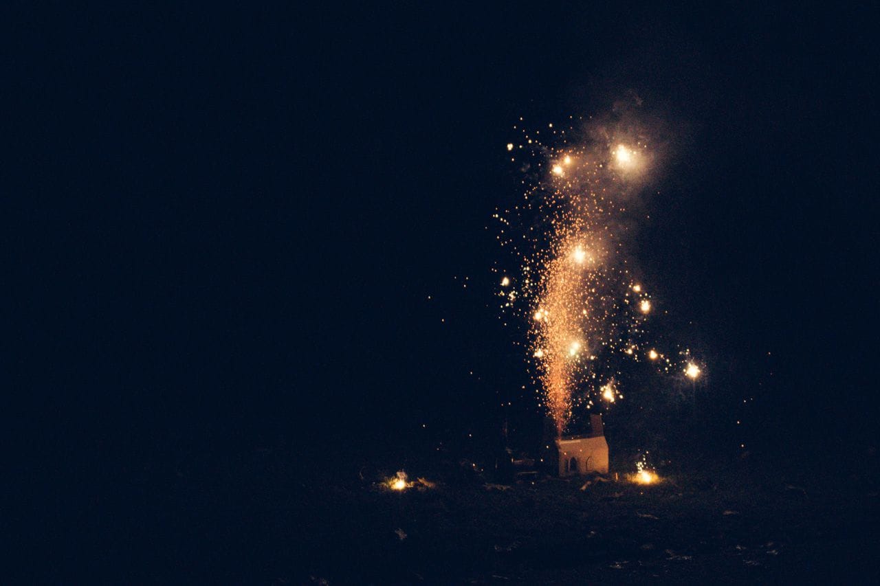 Fireworks shooting out of and illuminating the cardboard replica of the House of Lords again. Little sparks becoming temporary sources of light as they hit the grass on which it stands.