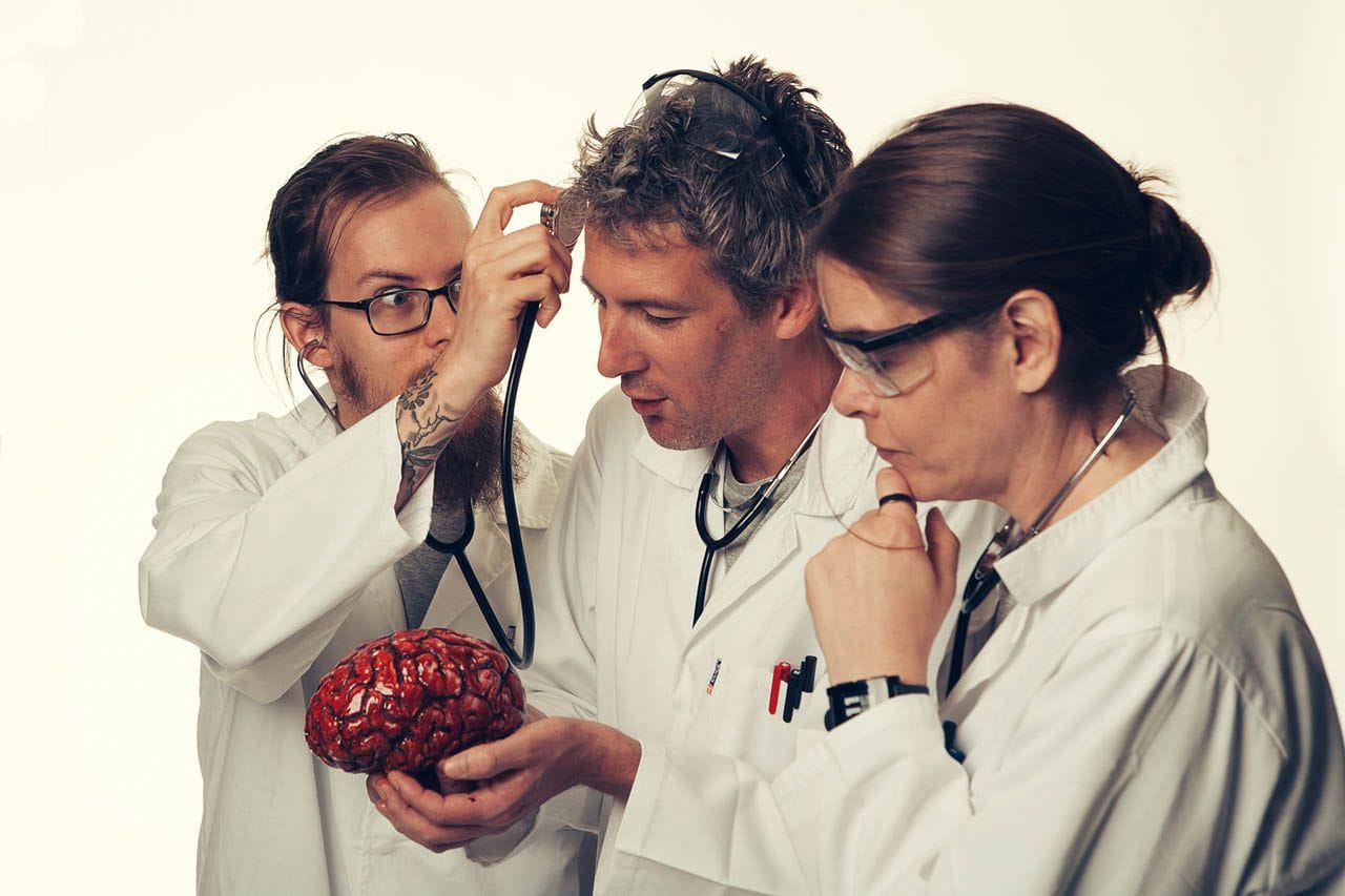 Carlos ignoring the brain in front of him and instead holding up a stethoscope to Kris's forehead.