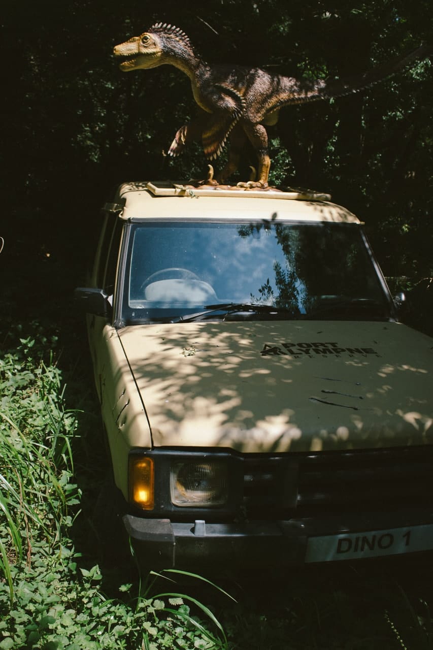 A dinosaur perched atop a broken down safari truck.