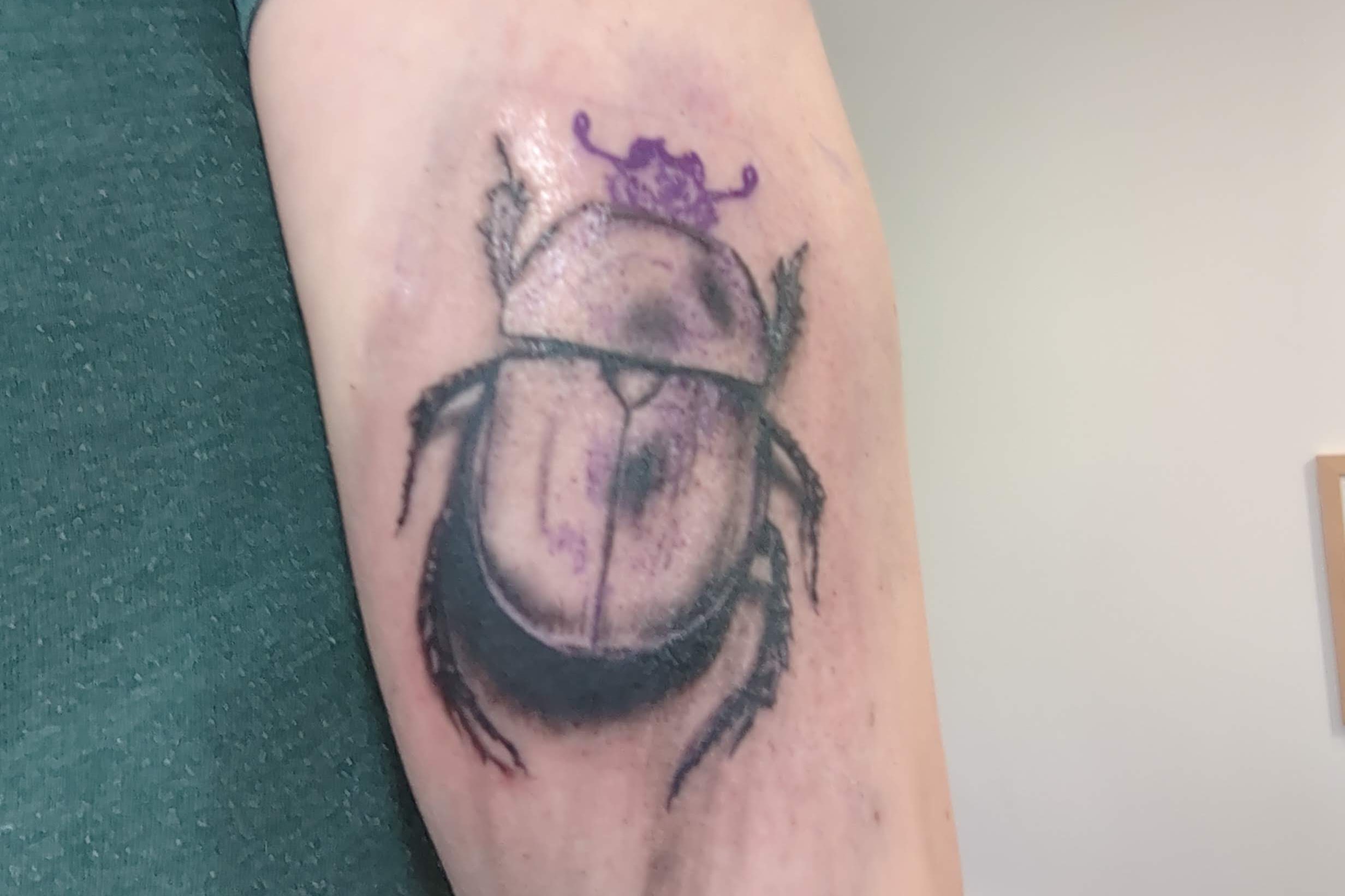 Closeup of a scarab tattoo in progress. The tattoo is mainly black outlines and some of the purple transfer can still be seen.
